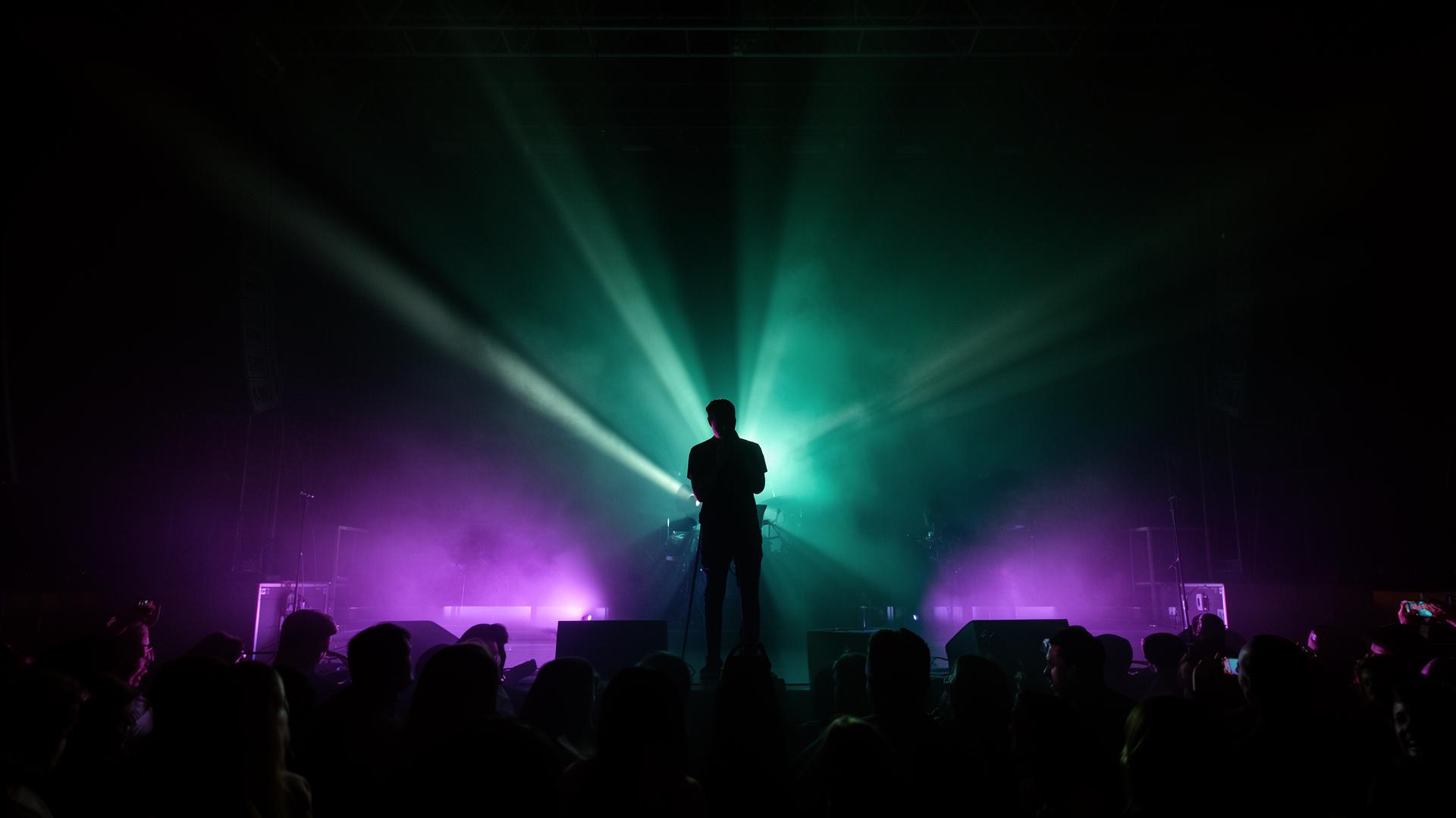Performer silhouetted in teal and purple stage lights